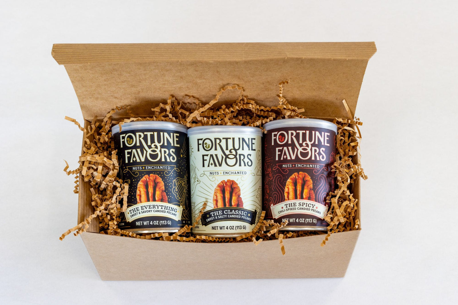 Three 4oz cans of Fortune Favors candied pecans lined up in a kraft gift box